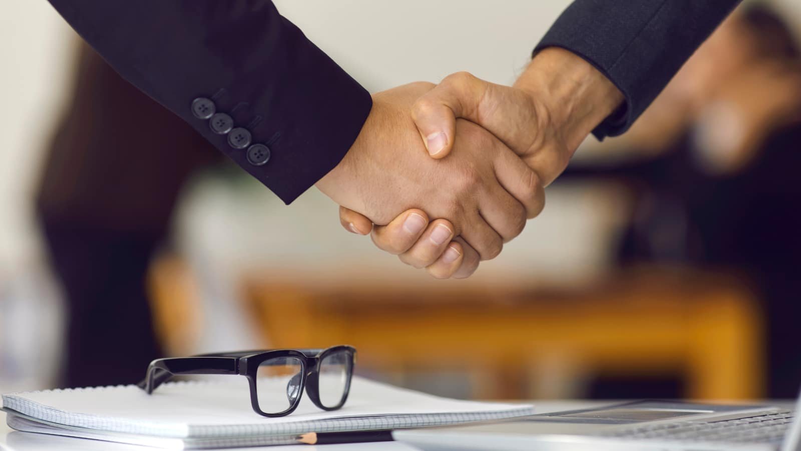 AI w HR – rekrutacja i proces zatrudnienia wspierany sztuczną inteligencją Uścisk dłoni nad biurkiem rekrutera symbolizujący zakończenie rozmowy kwalifikacyjnej i wykorzystanie AI w procesie rekrutacji