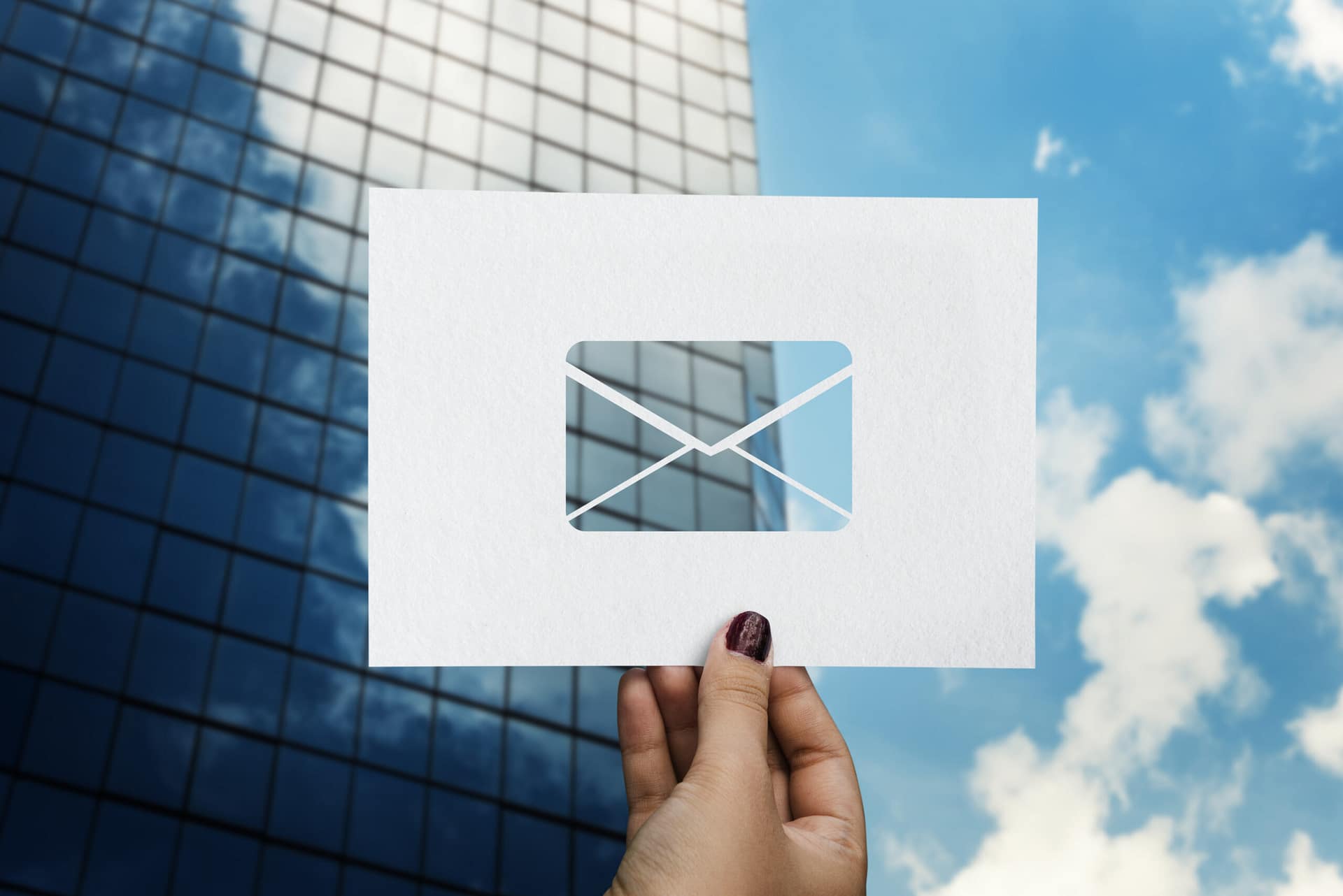 Building an email list with AI — a woman's hand holding a paper letter with an envelope symbol against an office building and sky