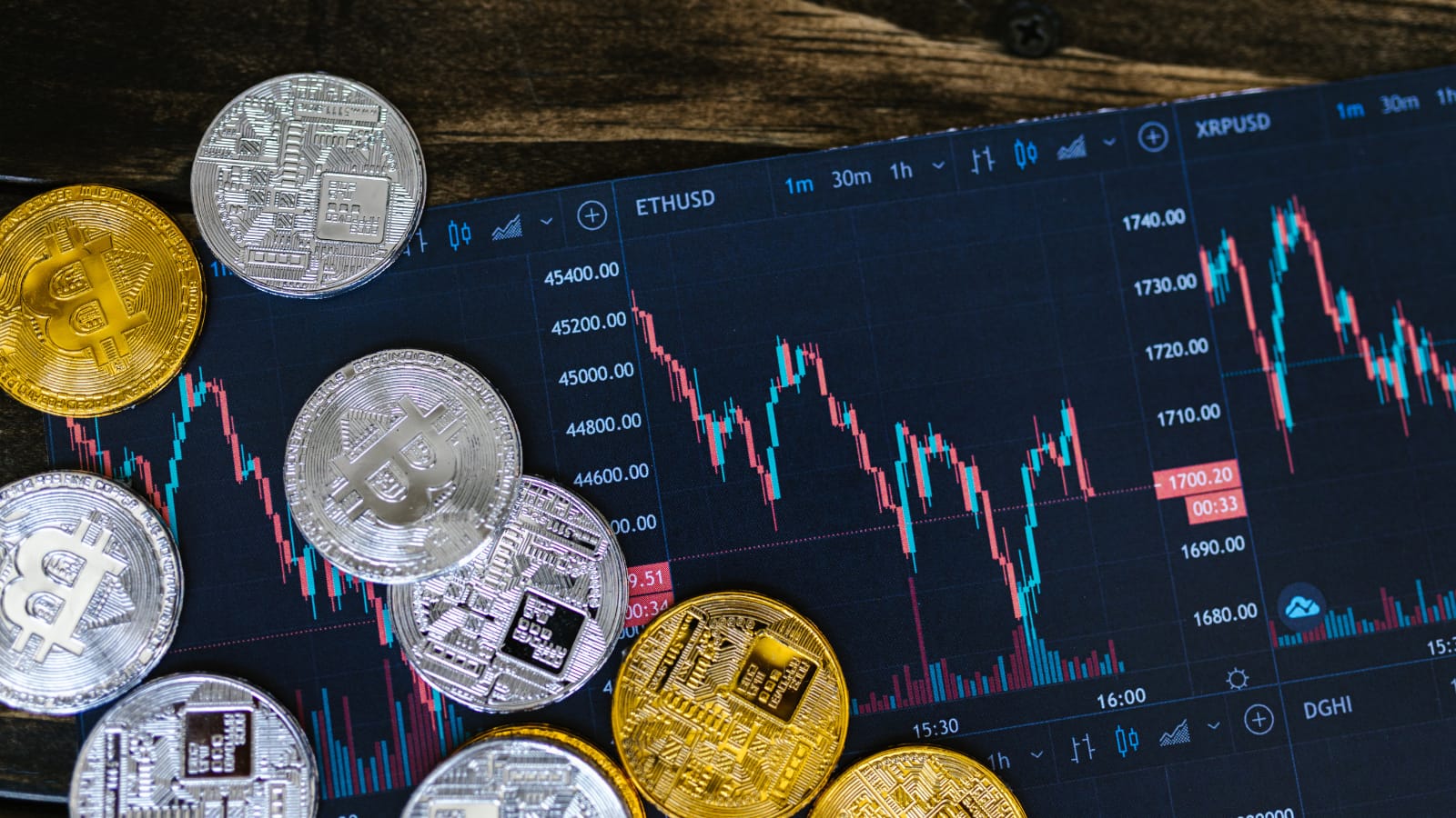 Monety z symbolami kryptowalut rozsypane na stole obok ekranu komputera wyświetlającego wykresy kursów walut, ilustrujące zarabianie z AI i Web3